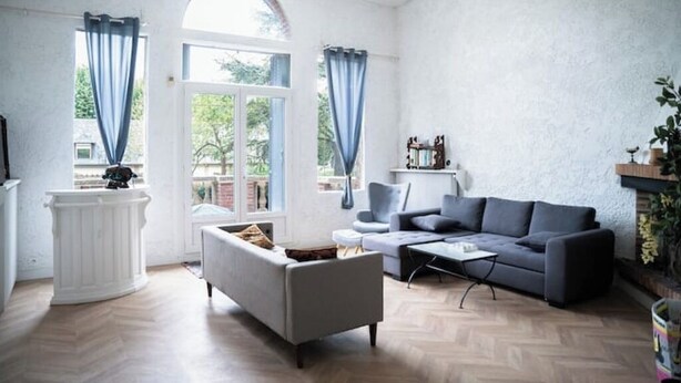 A living room with a grey sofa, a white armchair, a coffee table, and a white console table. There are two windows with blue curtains, and a fireplace with a mantel. - Large 10-bedroom manor house, sleeps up to 20—view of the Seine, Les Andelys, 1 hour from Paris (Les Andelys)