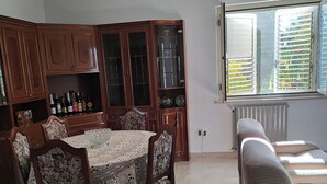 Un coin repas avec une table ronde et des chaises à motifs floraux, des meubles en bois et une fenêtre avec des stores.
