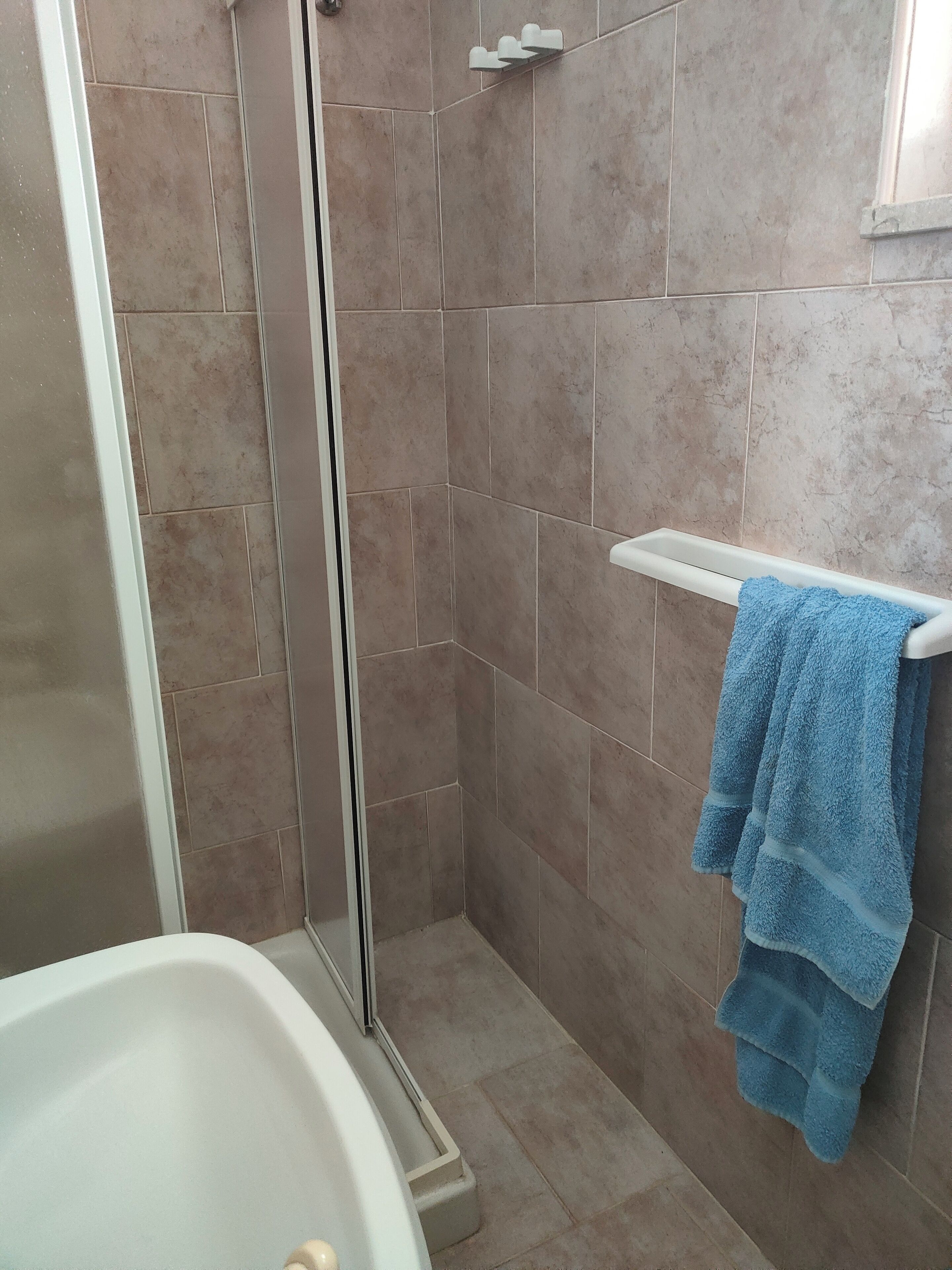 A bathroom with a shower, a bathtub, and a towel rack with a blue towel.
