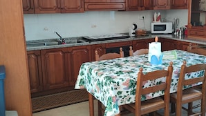 Une cuisine avec des meubles en bois, une table à manger recouverte d’une nappe à motifs floraux et un four à micro-ondes.