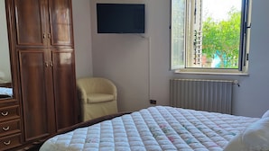Une chambre à coucher avec un grand lit, une armoire, une chaise, un téléviseur et une fenêtre donnant sur un paysage verdoyant.