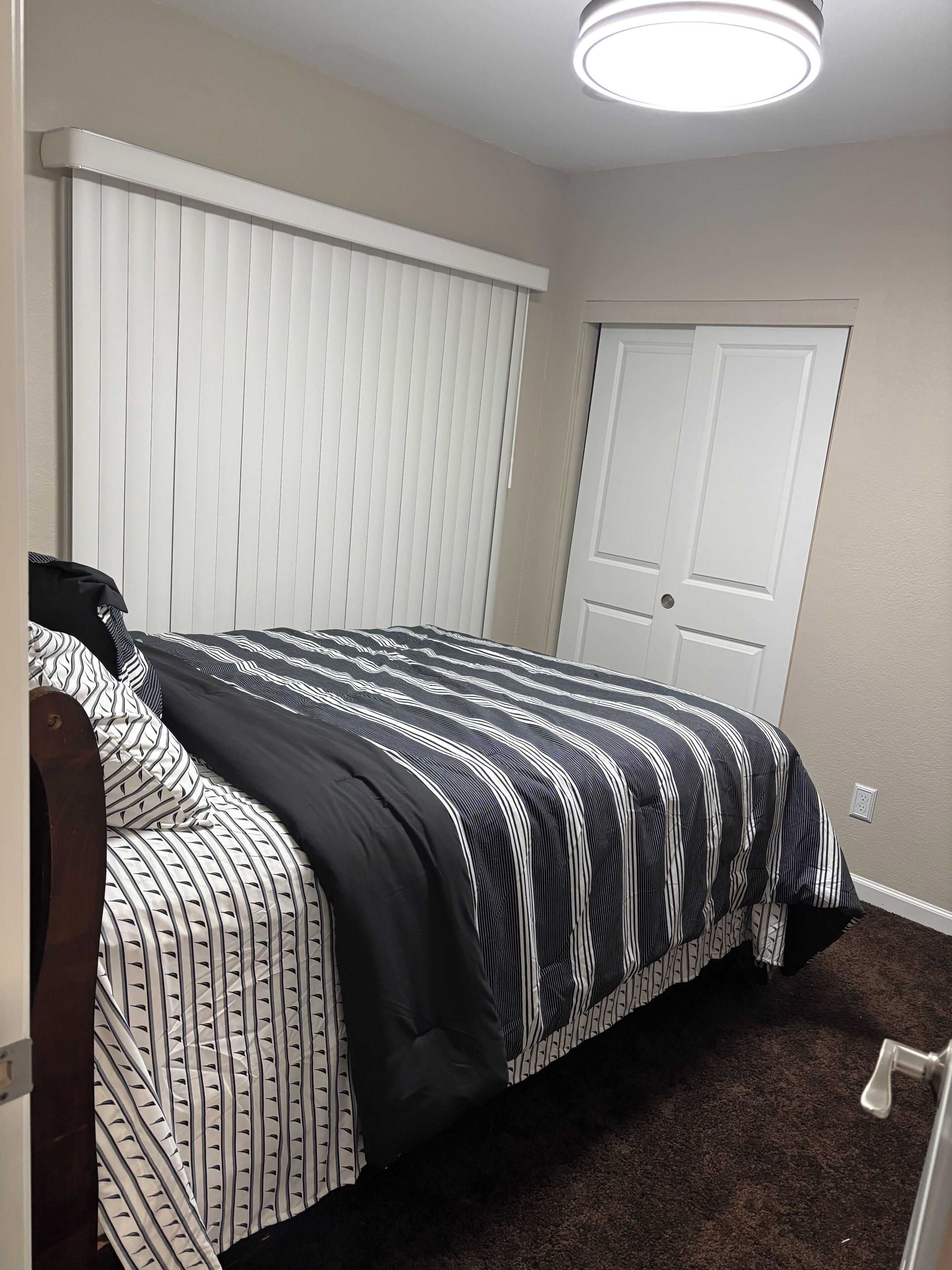 Un dormitorio con una cama, cabecera blanca, una puerta y una lámpara en el techo.