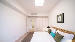 Une chambre avec un grand lit, une table de chevet avec une lampe, un tableau encadré au mur et une porte donnant sur une autre pièce.