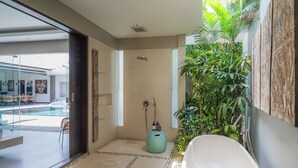 Een moderne badkamer met een vrijstaand bad, een douche en een grote potplant.