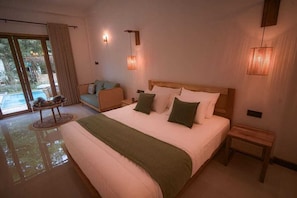 A spacious bedroom with a large bed, a small table, and a view of a pool.