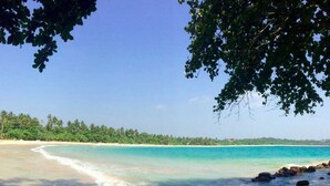A beach with clear turquoise waters, sandy shore, and a line of rocks in the foreground.