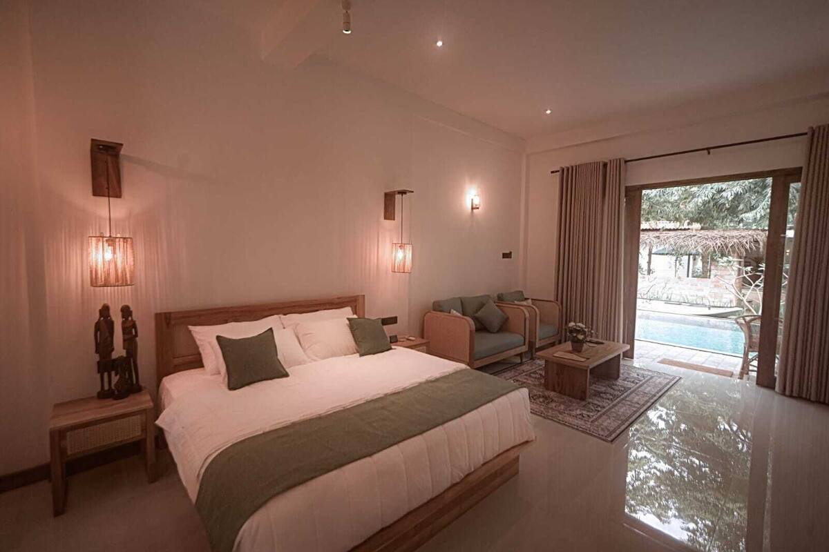 A spacious bedroom with a large bed, a sofa, and a view of a swimming pool.