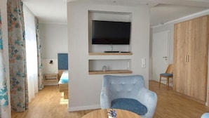 Una sala de estar moderna con un televisor de pantalla plana montado en la pared, un sillón azul, una mesa de centro de madera y un armario de madera.