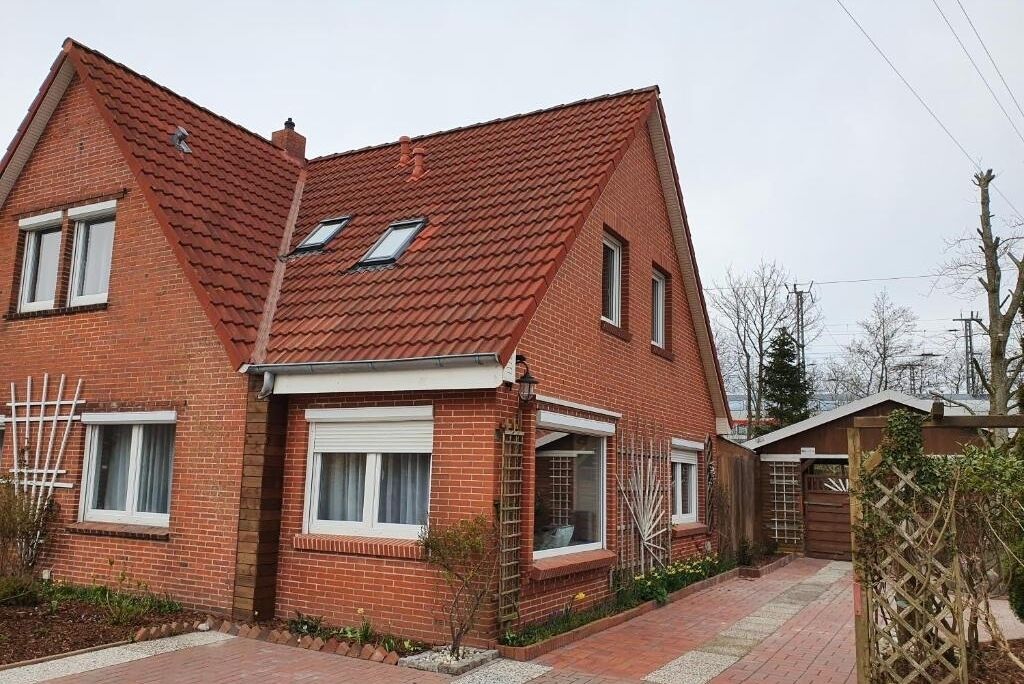 Une maison à deux étages, construite en briques, avec un toit recouvert de tuiles rouges, de nombreuses fenêtres et un petit jardin.
