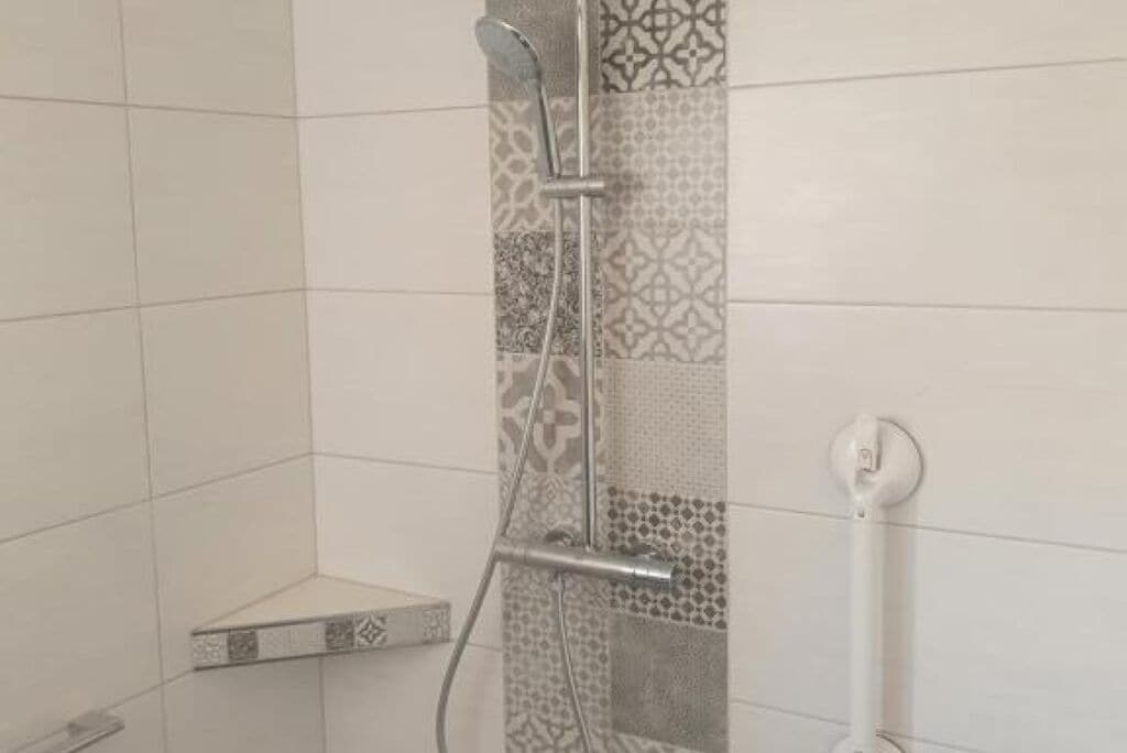 A shower with a handheld showerhead and a wall-mounted faucet.