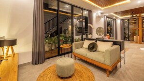 A modern living room with a sofa, ottoman, and a staircase leading to an upper level. - Villa Temple Tree By Soobali - UBUD (Ubud)