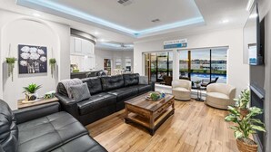 A modern living room with a black leather sofa, wooden coffee table, and a view of a pool and cityscape. - Lake it easy, Fish, Kayak, Yard, Boat, Sleeps 20 (Montgomery)