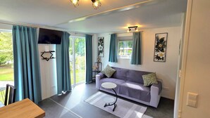 A modern living room with a sofa, a small round table, and a TV mounted on the wall. - Cottage Évasion (Chamoson)