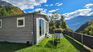 A cabin with a small patio, a table and chairs, and a view of mountains and trees. - Cottage Évasion (Chamoson)