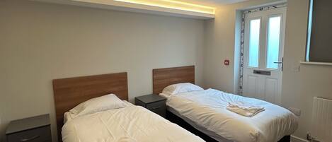 A hotel room with two beds, a nightstand, a radiator, and a window with curtains.