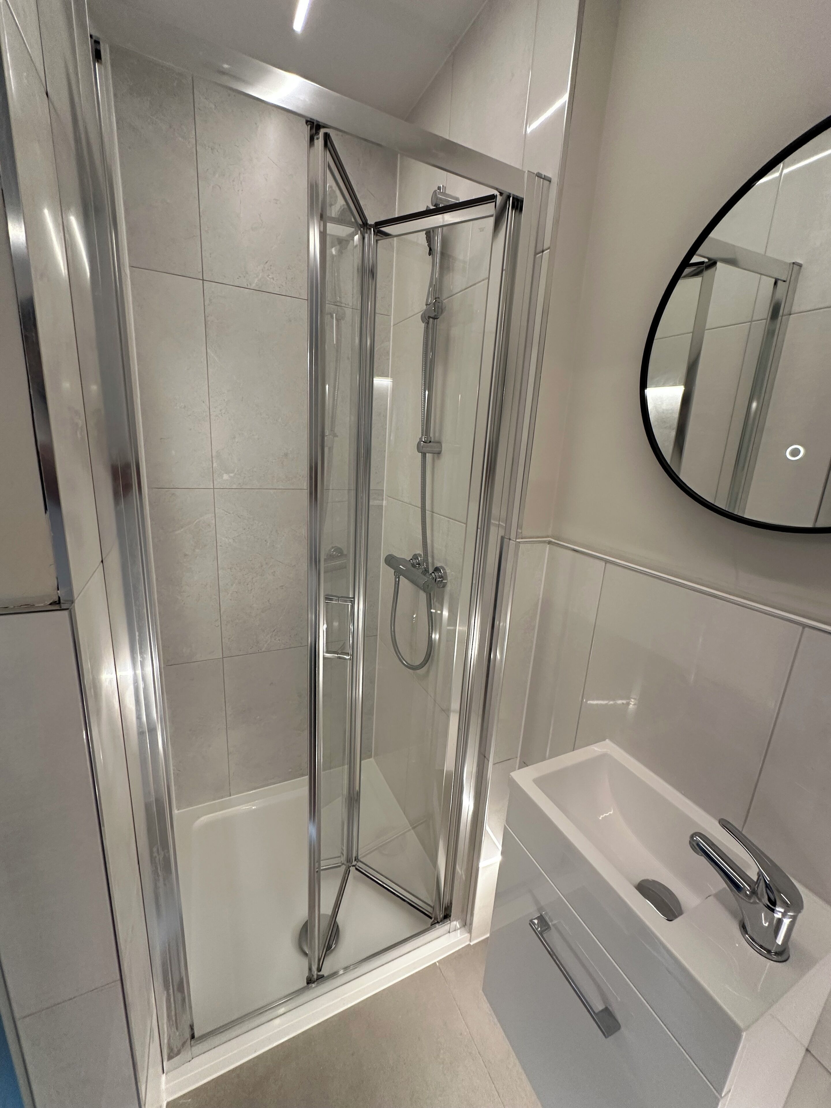 Une salle de bain moderne avec une douche à parois de verre, un lavabo blanc et un miroir.