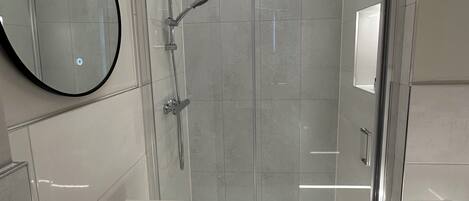 Un baño moderno con ducha de vidrio, espejo redondo y lavamanos blanco.