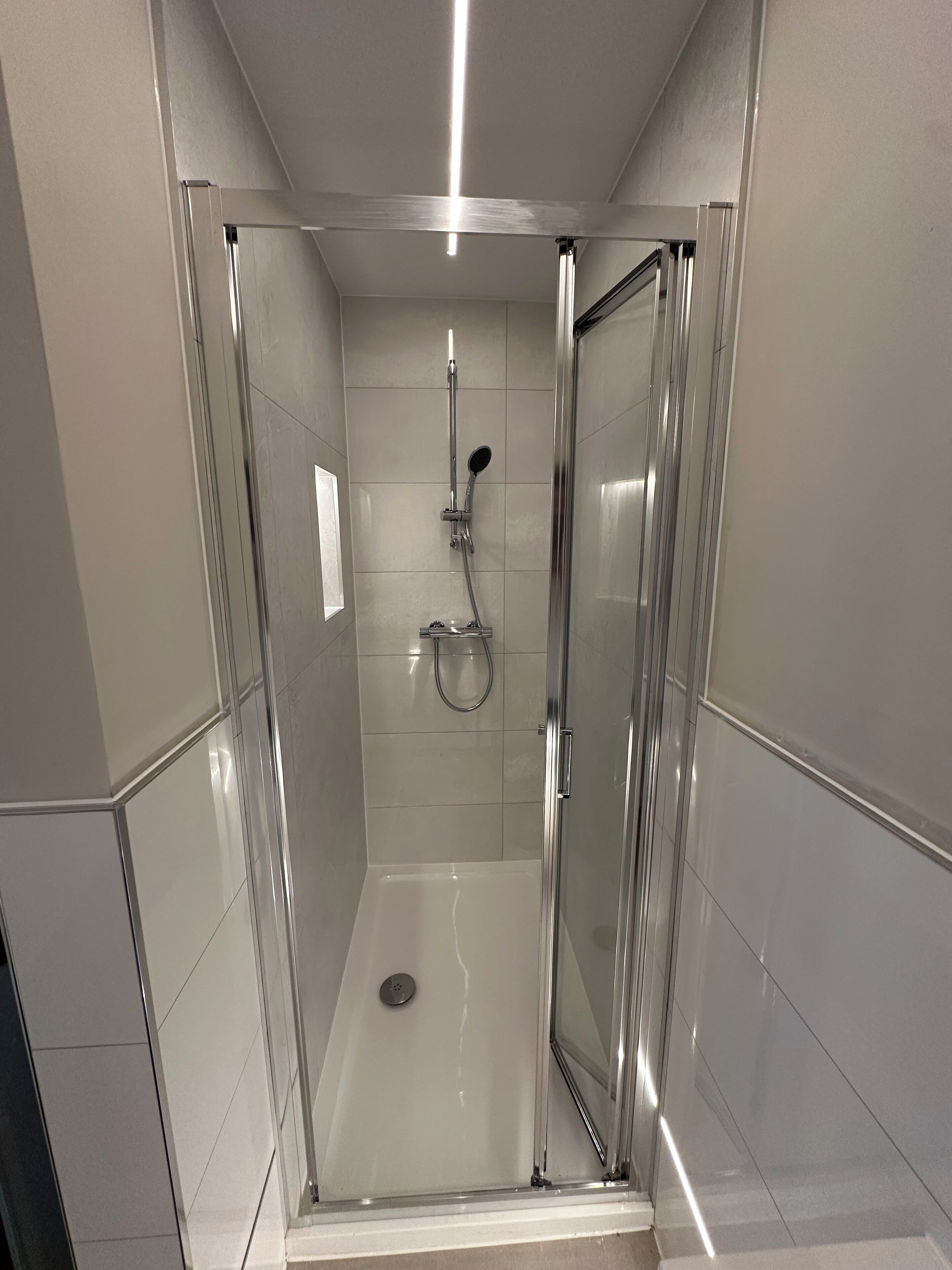 A modern, enclosed shower area with a glass door, a handheld showerhead, and a wall-mounted faucet.