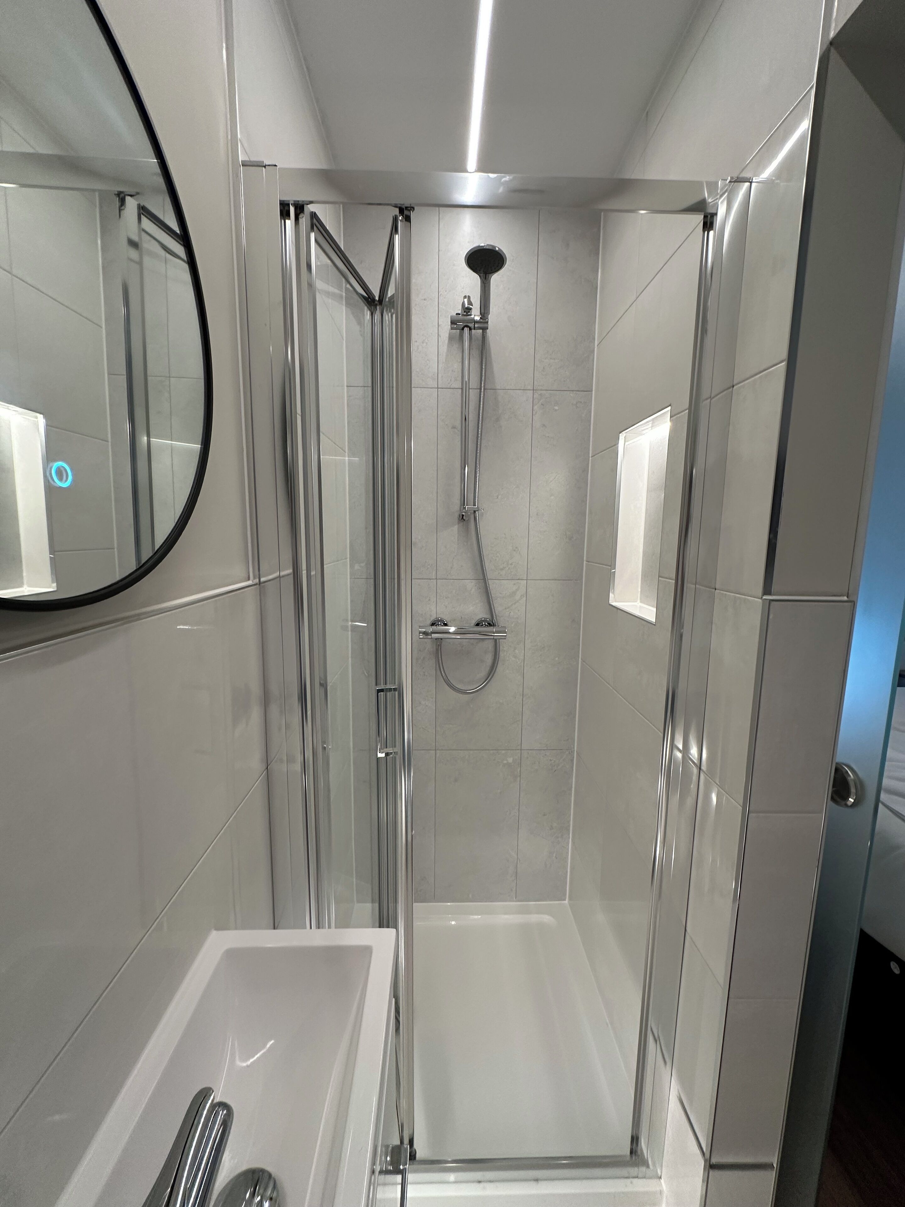 A modern bathroom with a glass-enclosed shower, a white bathtub, and a mirror on the wall.