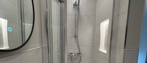 Un baño moderno con ducha envuelta en vidrio, una bañera blanca y un espejo en la pared.