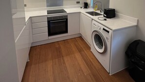 A modern kitchen with white cabinetry, a built-in oven, a washing machine, and a coffee maker. - Buckingham Annexe (High Wycombe)