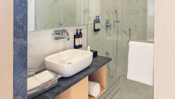 Ein modernes Badezimmer mit einer gläsernen Duschkabine, einem weißen Waschbecken und einer Marmorarbeitsplatte.