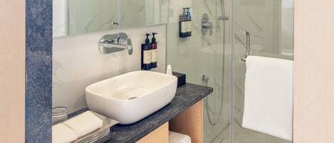 Un baño moderno con ducha envuelta en vidrio, un lavabo blanco y encimera de mármol.