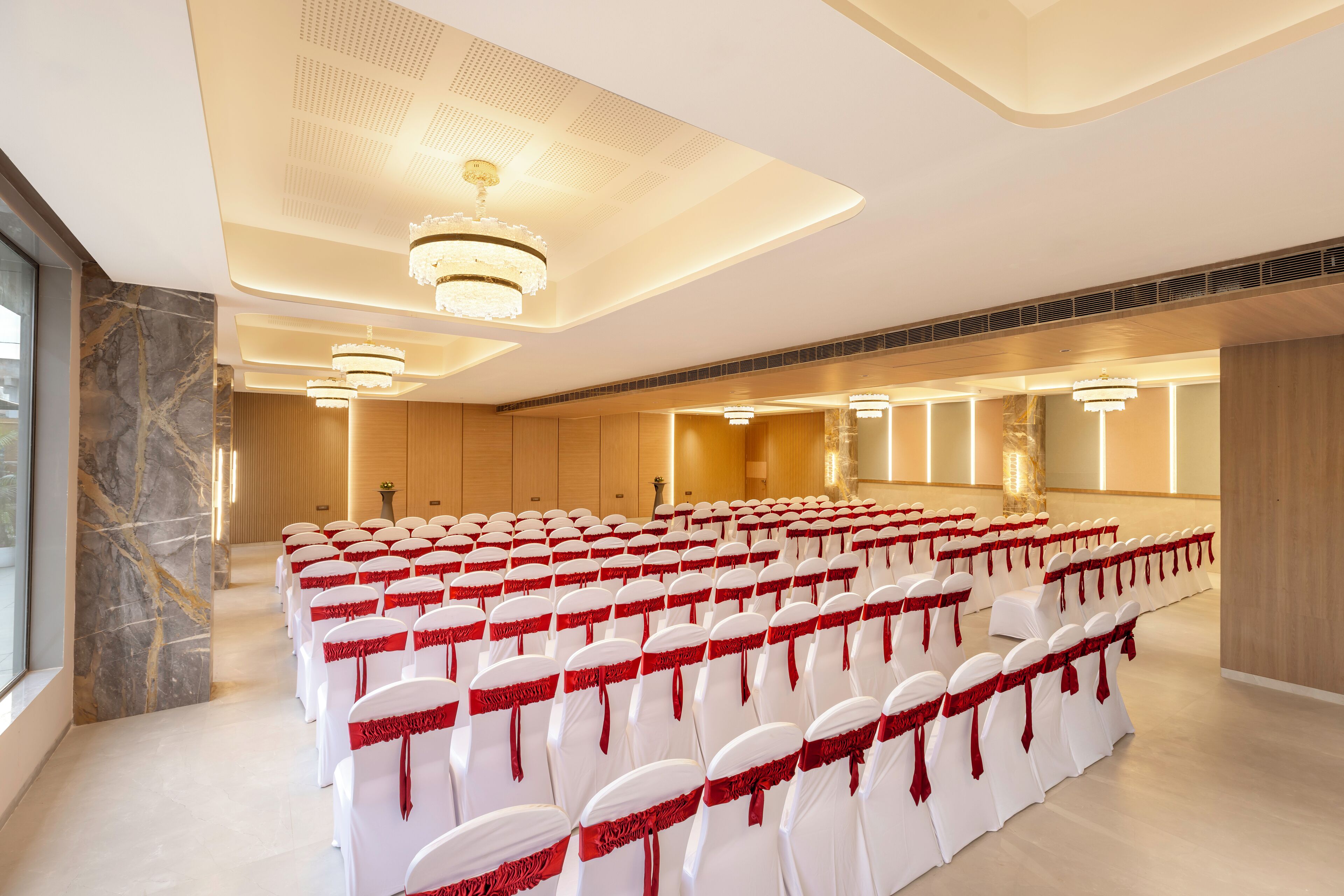 A conference room with rows of white chairs with red sashes, a marble wall, and a chandelier.