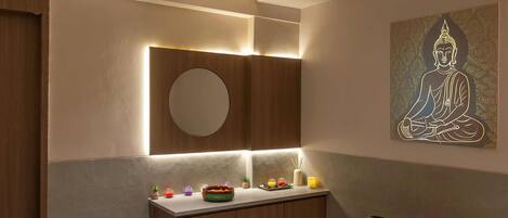 A modern spa room with a massage table, a small round mirror, a sink, and a meditation artwork on the wall.
