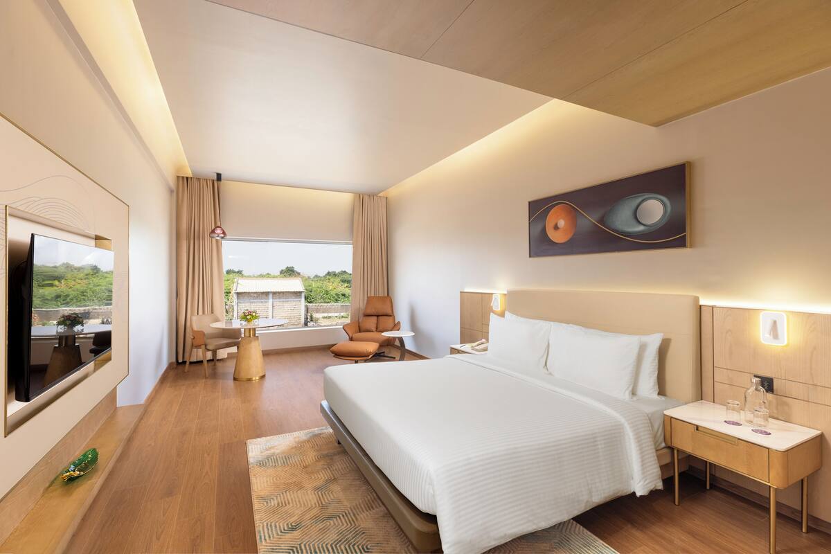 Moderni hotellihuone, jossa on suuri sänky, taulutelevisio, työpöytä ja näkymä vehreään maisemaan.