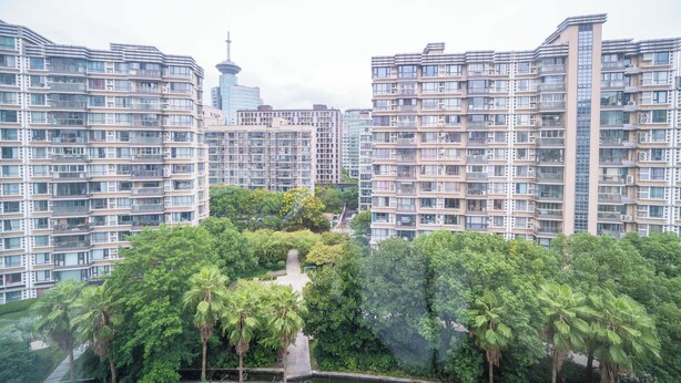 Un edificio residencial de gran altura con varios balcones, rodeado de vegetación exuberante y un parque central.
