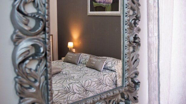 A bedroom with a large ornate mirror, a bed with patterned bedding, a nightstand with a lamp, and a framed picture of the moon on the wall. - Gabri's House has 3 rooms with 3 private bathrooms and a kitchen available (Rozzano)