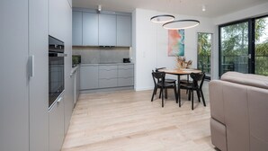 Een moderne keuken met grijze kastjes, een inbouwoven en een eethoek met een ronde tafel en stoelen.