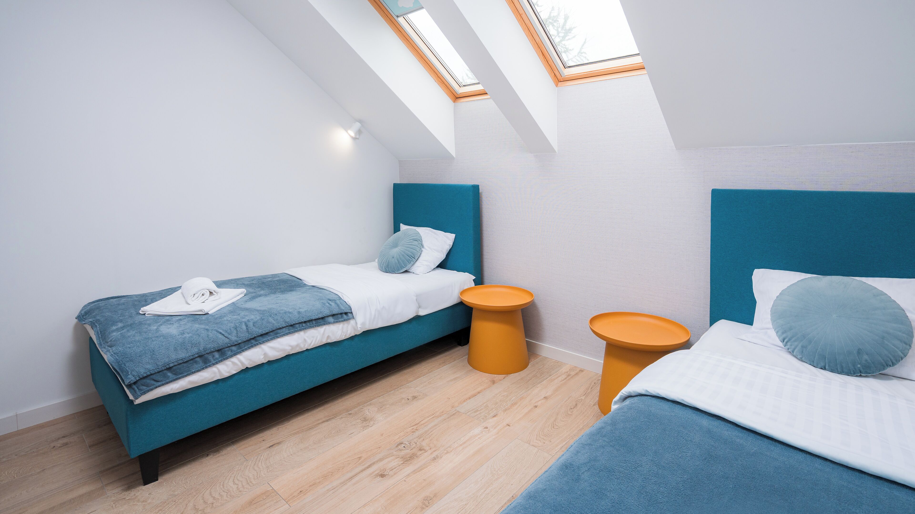 Ein modernes Schlafzimmer mit zwei Betten, einem Oberlicht und einem kleinen orangefarbenen Nachttisch.