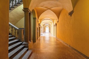 Un long couloir voûté, avec un escalier sur la gauche et une porte au fond.
