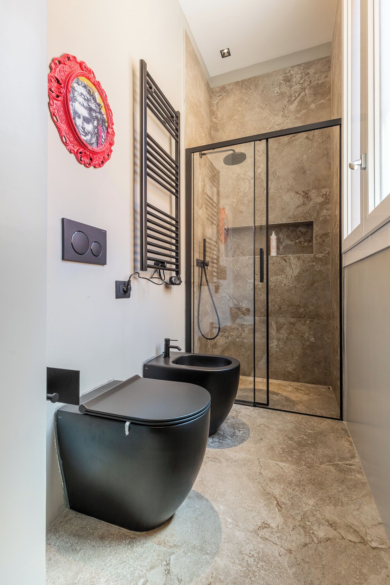 A modern bathroom with a glass shower enclosure, a black sink, and a red decorative mirror.