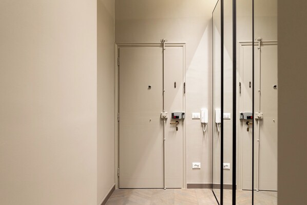 Un couloir avec deux portes, chacune dotée d’une serrure et d’un trou de serrure. Des prises de courant et des interrupteurs sont fixés aux murs.