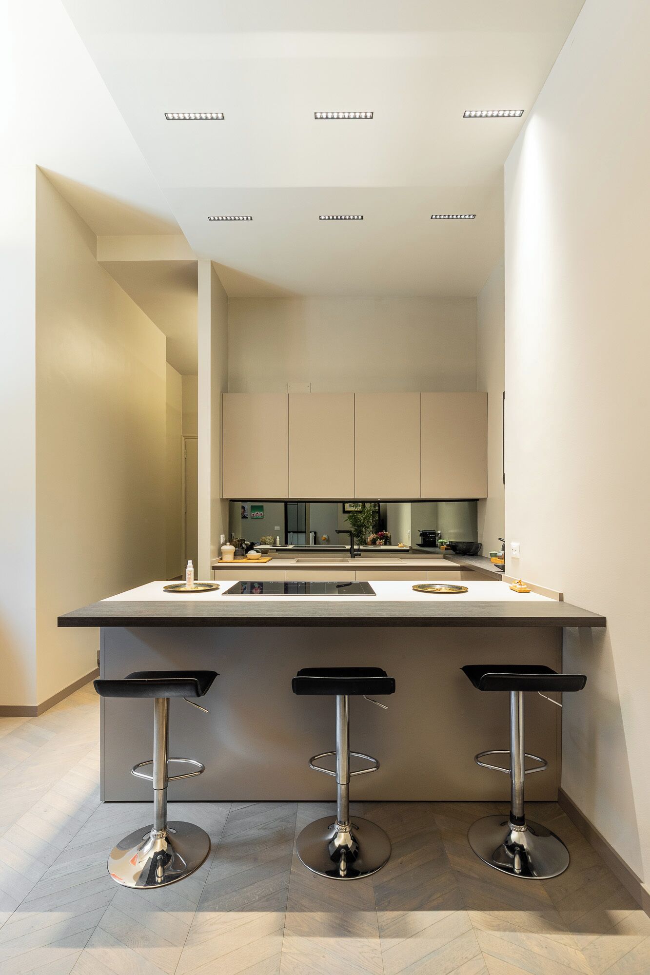 A modern kitchen with a central island, three bar stools, and built-in cabinets.