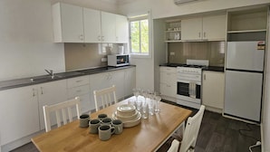 Une cuisine moderne avec des meubles blancs, une table à manger en bois et un four encastré.