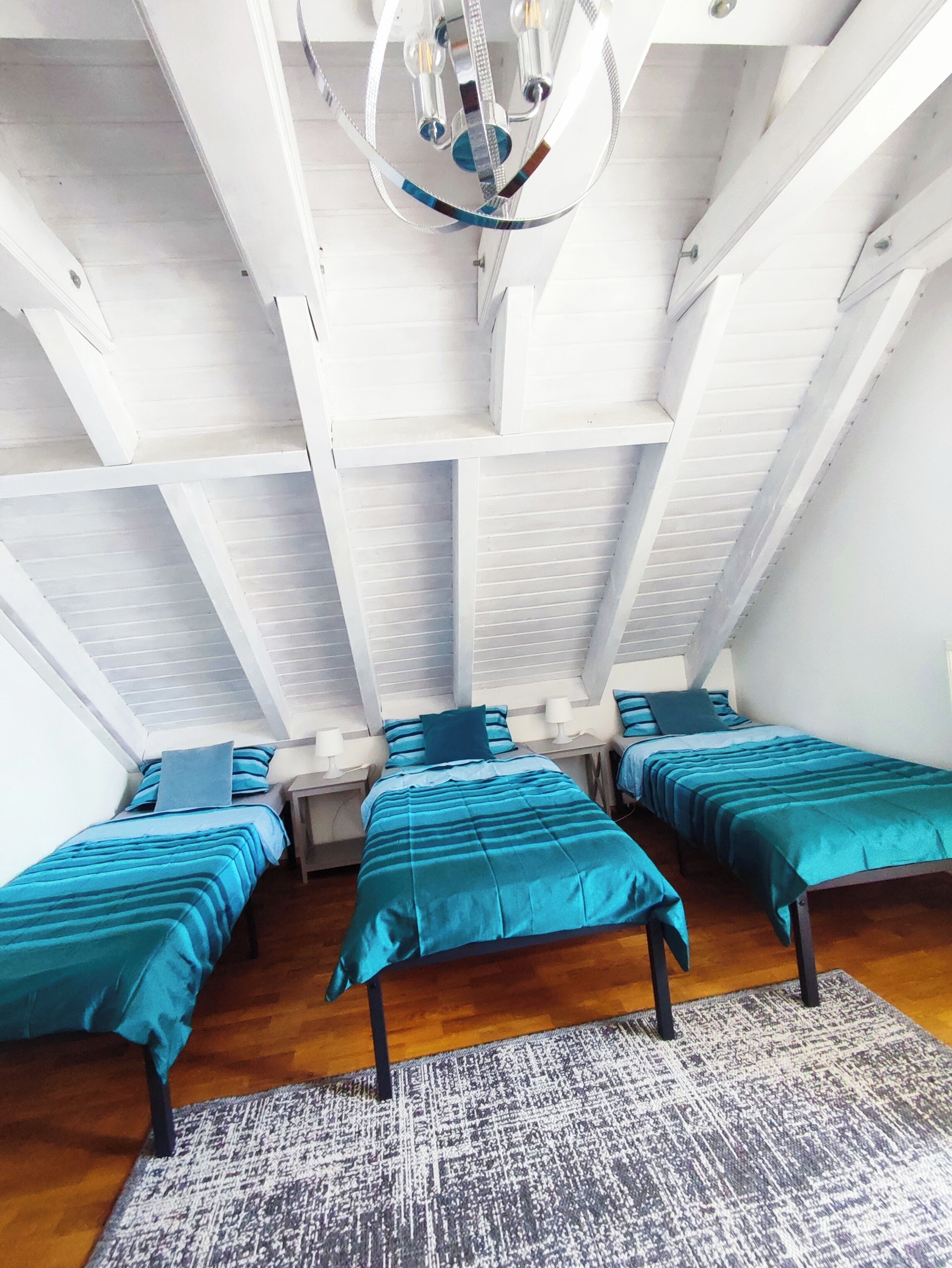 A room with three beds, a patterned rug, and a chandelier.