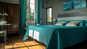 Een slaapkamer met een bed, een raam, een schilderij en een tafel met bloemen.
