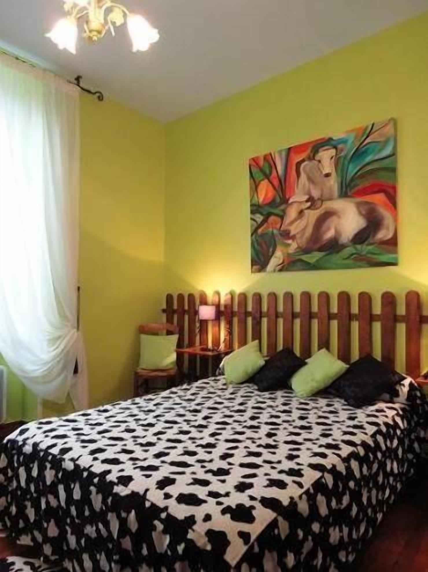 Une chambre avec un lit, une tête de lit en bois, un tableau au mur et une fenêtre avec des rideaux.