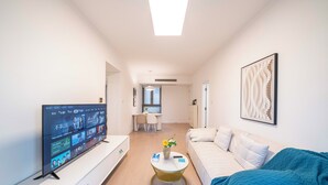 A modern hotel room with a flat-screen TV, a round coffee table with a vase, a sofa, and a bed. - Tyms Stylish 1BR APT  Yucui Garden (Shanghai)