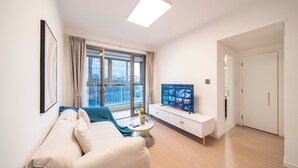 A modern living room with a sofa, a coffee table, a TV, and a large window with curtains. - Tyms Stylish 1BR APT  Yucui Garden (Shanghai)
