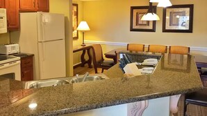 A kitchen with granite countertops, a refrigerator, a microwave, and a dining area with a table and chairs. - 4th of July Near Disney (Lake Buena Vista)