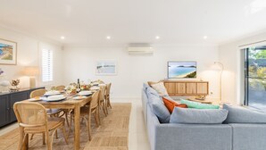 A modern living room with a dining area, featuring a sofa, dining table, and chairs. - Capri Blue 2, 88 Tomaree Rd - stunning townhouse with Wi-Fi, Air Con (Shoal Bay)