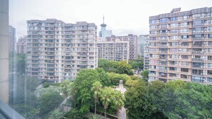 A high-rise residential building with multiple balconies, surrounded by lush greenery and other high-rise buildings.