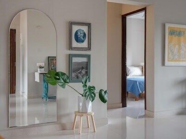 A room with a large mirror, a plant on a stool, and framed pictures on the wall.