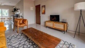 Una sala moderna con una mesa de centro de madera, un sofá, un televisor en un mueble y una lámpara.