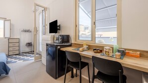 A compact kitchen with a microwave, refrigerator, and a small dining area with two chairs. A window provides a view of the cityscape. - Fiorelli 17 - Blue Peafowl Studio with Private Terrace and Wi-Fi (Palermo)